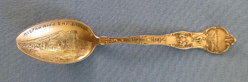 Souvenir Mining Spoon Mizpah Mine.JPG - SOUVENIR MINING SPOON MIZPAH MINE TONOPAH NV - Sterling silver souvenir demitasse spoon, features handle with miners and marked NEVADA, bowl withdetailed engraving of Mizpah mine scene and marked MIZPAH MINE & MT. BROUGHER at top and TONOPAH across bottom, length 4 1/8 in., marked on reverse Sterling and maker’s mark of S in a circle for Shepard Mfg. Co. MelroseHighlands, MA 1893-1923 (Mt. Brougher is a 6,500 ft. summit just to the west of Tonopah town) [Tonopah is an unincorporated town and the county seat of Nye County, Nevada. It is located approximately midway between Las Vegas and Reno.  One of the richest booms in the west occurred at Tonopah Springs on May 19, 1900. And the name Jim Butler will forever be associated with the name Tonopah and the many stories that surround the discovery. The legendary tale of discovery says that he went looking for a burro that had wandered off during the night and sought shelter near a rock outcropping. When Butler discovered the animal the next morning, he picked up a rock to throw at it in frustration, noticing that the rock was unusually heavy. He had stumbled upon the second-richest silver strike in Nevada history. News of the discovery traveled to the Klondike and soon scores of eager prospectors were searching the area. But it was not until August 27, 1900 that Butler and his wife filed on eight claims near the springs, six of which were some of the biggest producers the state has ever had including the Desert Queen, Burro, Valley View, Silver Top, Buckboard, and Mizpah, the largest silver producer in the district. Because the Butler claims were known far and wide, the town was often referred to as Butler. By the summer of 1901, the mines around the town produced nearly $750,000 worth of gold and silver. Now it was time for a post office and one opened on April 10, 1901 named Butler.  By 1902 Jim Butler had sold his claims, which were all consolidated and gave birth to a new company, the Tonopah Mining Company. It was incorporated in Delaware, with stock listed on both the Philadelphia and San Francisco exchanges. The company, with J.H. Whiteman as president, controlled 160 acres of mineral-bearing ground around the Tonopah district. The company also had holdings in the Tonopah-Goldfield Railroad and controlled mining companies in Colorado, Canada, California and Nicaragua. The mine workings at Tonopah consisted of three deep shafts with more than 46 miles of lateral workings. The deepest of the three shafts was 1,500 ft. The ore mined at the site was treated in a 100-stamp mill. Also in 1902 the Tonopah-Belmont Mining Company was formed and was based in New Jersey with C.A. Heller as president. The company’s property, 11 claims covering more than 160 acres, was on the east side of the property owned by the Tonopah Mining Company. There were two deep vertical shafts, 1,200 and 1,700 ft, with workings covering almost 39 miles.  Butler now had a population of 650 and was increasing every day. It also had six saloons, restaurants, assay offices, lodging houses, and a number of doctors and lawyers. It was not until March 3, 1905 that its name was changed to Tonopah. By 1907, Tonopah had become a full-fledged city with modern hotels, electric and water companies, five banks, schools, and hundreds of other buildings. Tonopah’s mines continued to produce extremely well until the Depression brought a slowdown. From 1900 to 1921, they produced ore worth almost $121 million. Tonopah’s biggest year was 1913 when its mines yielded almost $10 million worth of gold, silver, copper, and lead. By the time World War II started, only four major mining companies were operating in Tonopah. At the end of the war even the companies that had been there at the beginning were gone. In 1968, Howard Hughes and his Summa Corporation bought 100 claims in Tonopah, including the Mizpah, Silver Top, and Desert Queen mines. Hopes for a mining revival soon faded after disappointing core samples were taken. A few of the old mines were re-timbered but never reopened. The value of the Tonopah district’s total production is just over $150 million.  Today tourism plays a large part in the local economy.]